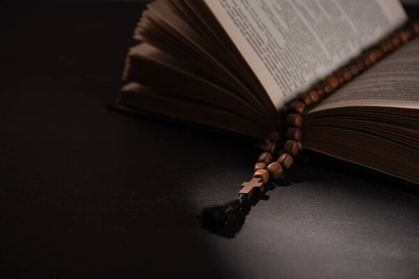 holy bible with rosary on black dark background with sunlight 