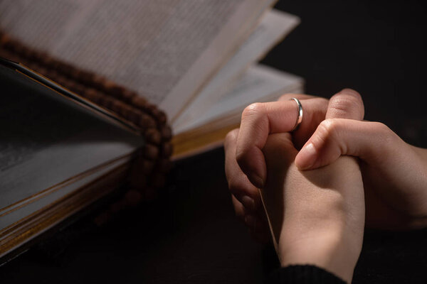 обрезанный вид женщины, молящейся возле святой библии с четками в темноте
