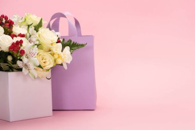 Çiçek buketi, pembe arka planda menekşe kese kağıdının yanındaki hediye kutusunda.