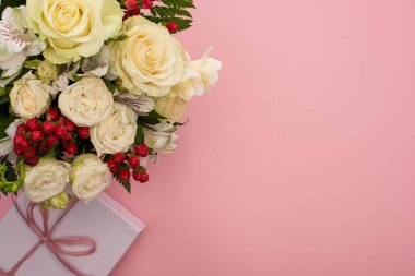 Çiçek demetinin en üst görüntüsü pembe arka planda fiyonklu bir hediye kutusunda.