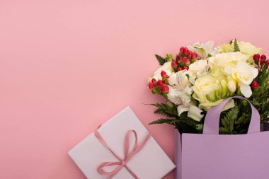 Pembe arka planda hediye kutusunun yanındaki menekşe kağıt çantanın içindeki çiçek buketinin üst görüntüsü