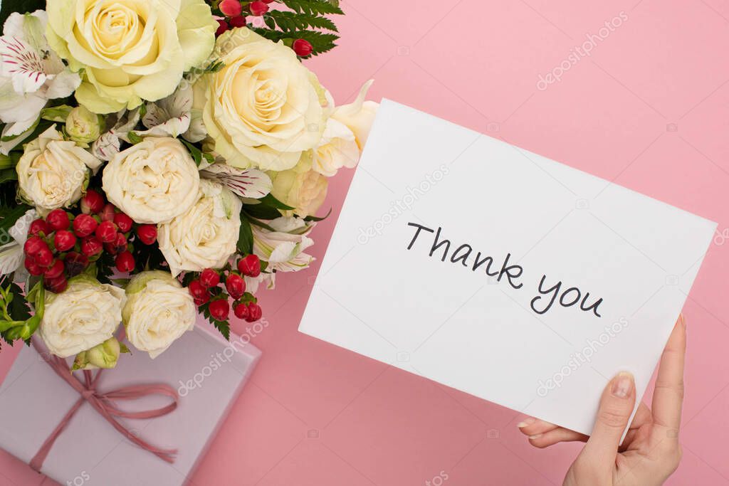 top view of bouquet of flowers near female hand with thank you card on pink background