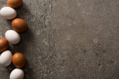 vrchní pohled na hnědé a bílé kuřecí vejce na šedém texturovaném pozadí