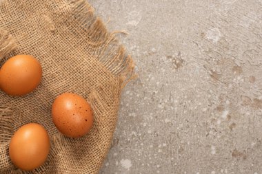 Gri çimento arka planda çuval bezinde kahverengi tavuk yumurtalarının üst görüntüsü