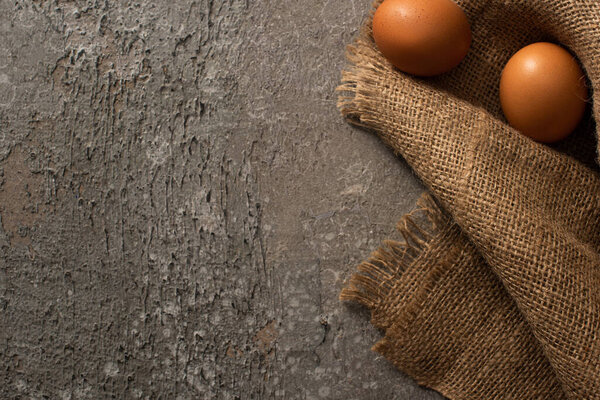 верхний вид коричневых куриных яиц на мешковину на сером бетонном фоне

