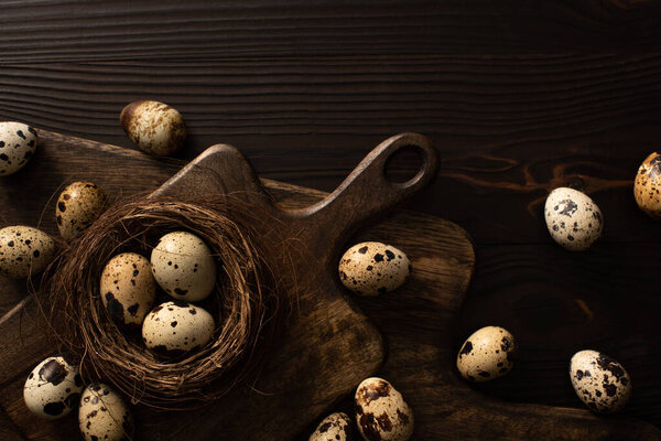 top view of quail eggs in nest and on brown cutting boards on dark wooden surface