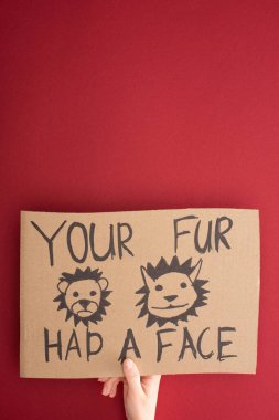 partial view of woman holding cardboard sign with your fur had a face inscription on red background clipart
