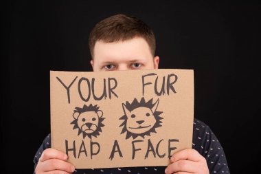 man with obscure face holding cardboard sign with your fur had a face inscription isolated on black clipart
