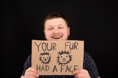 happy smiling man holding cardboard sign with your fur had a face inscription isolated on black clipart