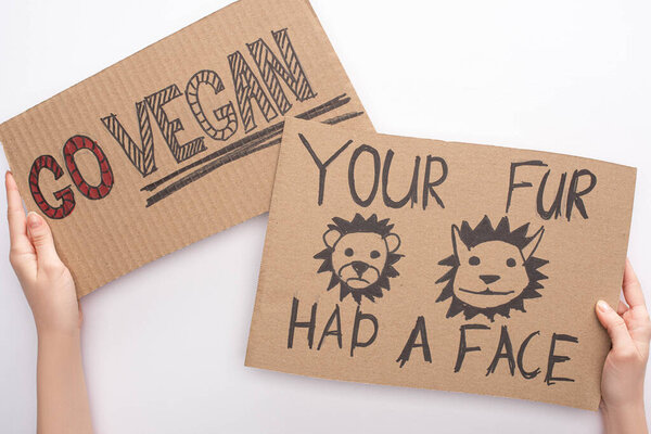 partial view of woman holding cardboard signs with go vegan and your fur had face inscriptions on white background