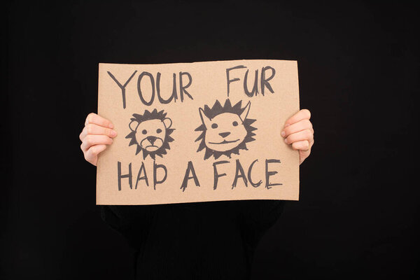 partial view of woman holding cardboard sign with your fur had a face inscription isolated on black