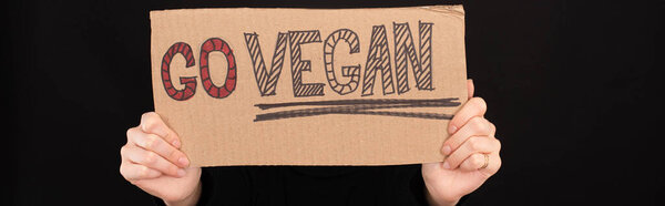 panoramic shot of woman holding cardboard sign with go vegan inscription isolated on black