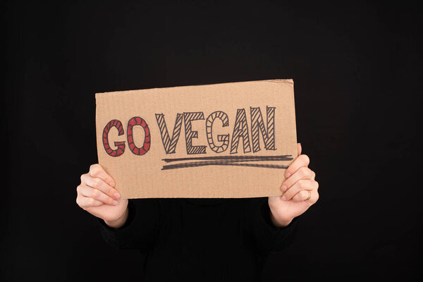 partial view of woman holding sign with go vegan inscription isolated on black