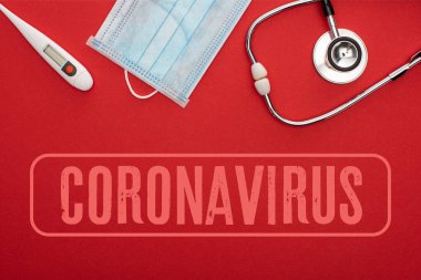 Kırmızı zemin üzerinde termometre ve steteskop ile Coronavirus illüstrasyonlu tıbbi maskenin üst görüntüsü