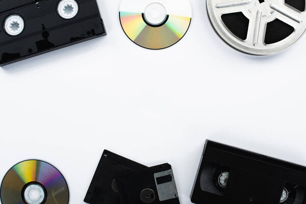 top view of CD discs, VHS cassettes, film reel and diskettes on white background