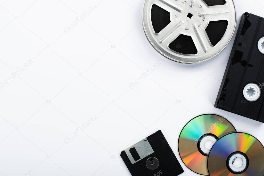 top view of CD discs, black VHS cassette, diskette and film reel on white background
