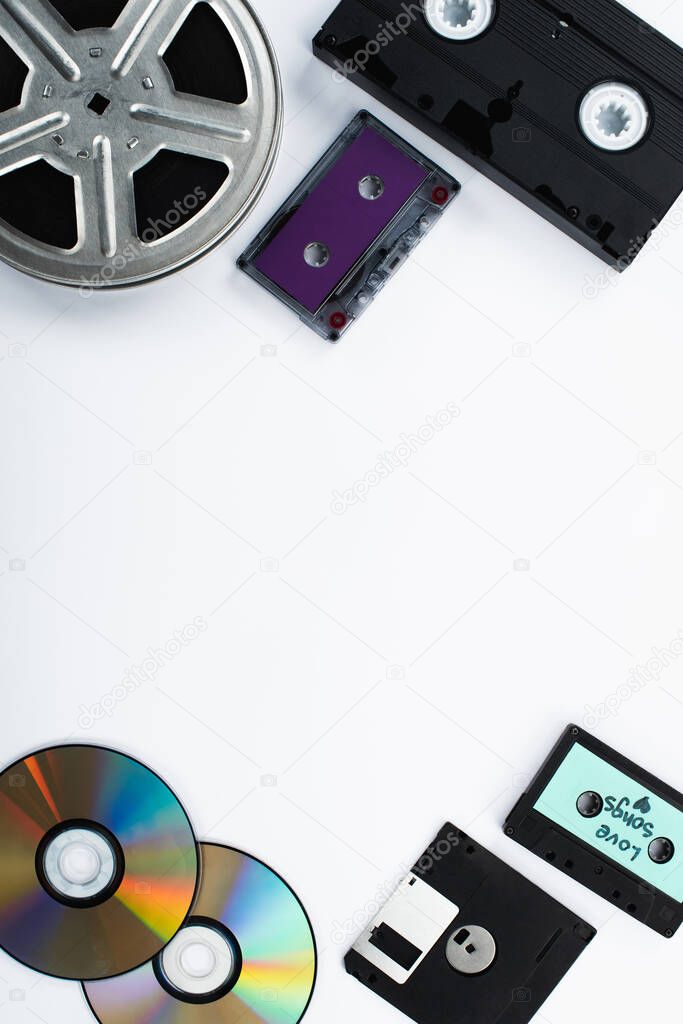 top view of CD discs, cassettes, VHS cassette, diskette and film reel on white background
