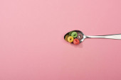 top view of bright colorful breakfast cereal in spoon on pink background