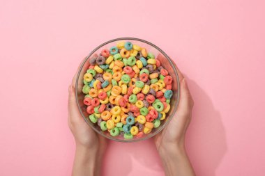 cropped view of woman holding bright colorful breakfast cereal in bowl on pink background clipart