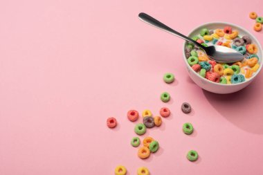 Parlak renkli kahvaltı gevreği, kasede süt ve pembe arka planda kaşık.