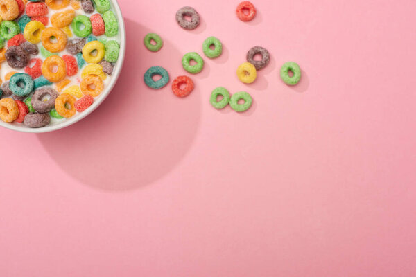 top view of bright colorful breakfast cereal with milk in bowl on pink background