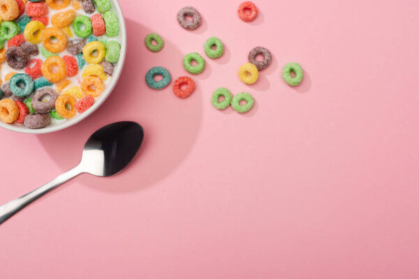 top view of bright colorful breakfast cereal with milk in bowl near spoon on pink background