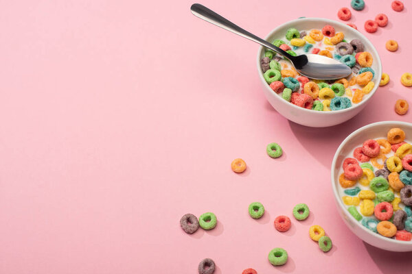 bright colorful breakfast cereal with milk in bowls with spoon on pink background