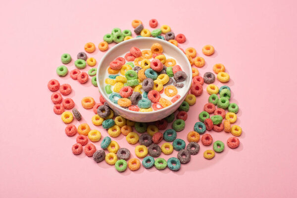 bright colorful breakfast cereal with milk in bowl and around on pink background