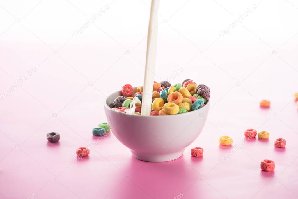 bright multicolored breakfast cereal in bowl with pouring milk on pink background