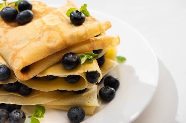 close up view of tasty crepes with mint and blueberries on plate on white background clipart