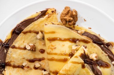 top view of tasty crepes with chocolate spread and walnuts on plate on white background clipart