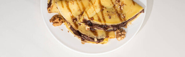 вид сверху на вкусные блины с шоколадом и орехами на тарелке на сером фоне, панорамный снимок
