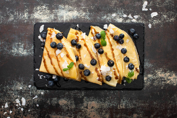 вид сверху на вкусные блины с черникой, мятой и кокосовыми хлопьями, подаваемые на борту на текстурированном фоне
