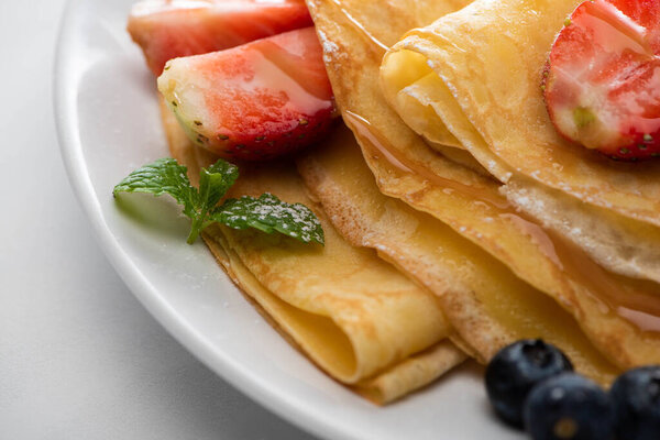 close up view of tasty crepes with blueberries, strawberries and mint on plate