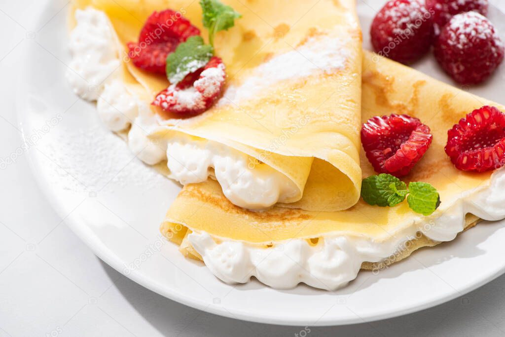 close up view of tasty crepes with raspberries and whipped cream on plate