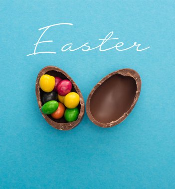 Top view of chocolate Easter egg halves with colorful sweets on blue background with Easter illustration clipart