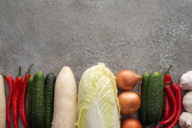 top view of chili peppers, cucumbers, daikon radish, chinese cabbage, onions and garlic on grey concrete background clipart