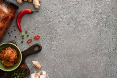 Kavanozda kimchi ve beton yüzeyde zencefil, sarımsak ve kırmızı biber yanında kase.