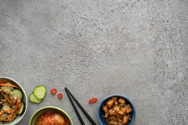 Dilimlenmiş salatalık ve beton yüzeyde yemek çubukları olan lezzetli kimchi tabakları.