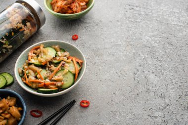 Tabaklarda lezzetli kimchi ve beton yüzeyde yemek çubuklarının yanında kavanozlar.