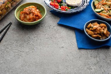 Tabaklarda lezzetli kimchi ve beton yüzeyde çubukların yanında mavi bez üzerinde kavanoz. 