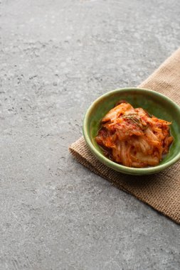 Bir kase lezzetli Kore kimchi 'si ve beton yüzeyde çuval bezi.