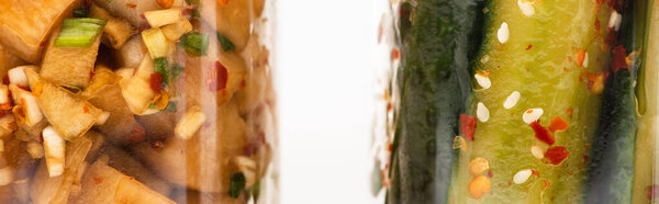 panoramic shot of cucumber and daikon radish kimchi in glass jars isolated on white
