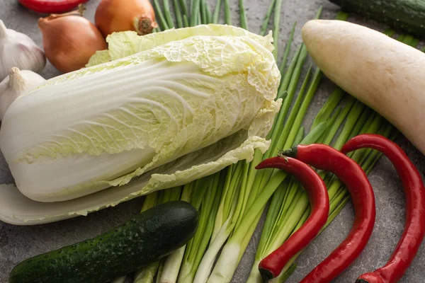 top view of chinese cabbage, chili peppers, cucumbers, onions, daikon radish and green onions on concrete surface