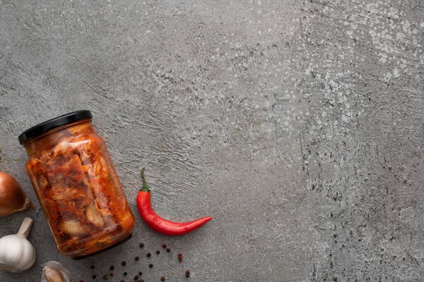 top view of kimchi jar, chili pepper and garlic on concrete surface