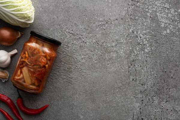 top view of kimchi jar, chili peppers, garlic, onions and chinese cabbage on concrete background