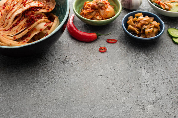 bowls with tasty kimchi near chili pepper and garlic on concrete surface