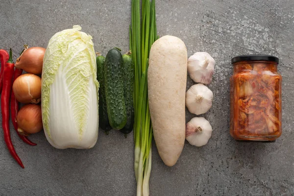 Top view of chili peppers, kimchi jar, green onions, cucumbers, daikon radish, chinese cabbage, onions and garlic on grey concrete background — Stock Image Top View Chili Peppers Kimchi Jar Green Onions Cucumbers Daikon Royalty Free Stock Images