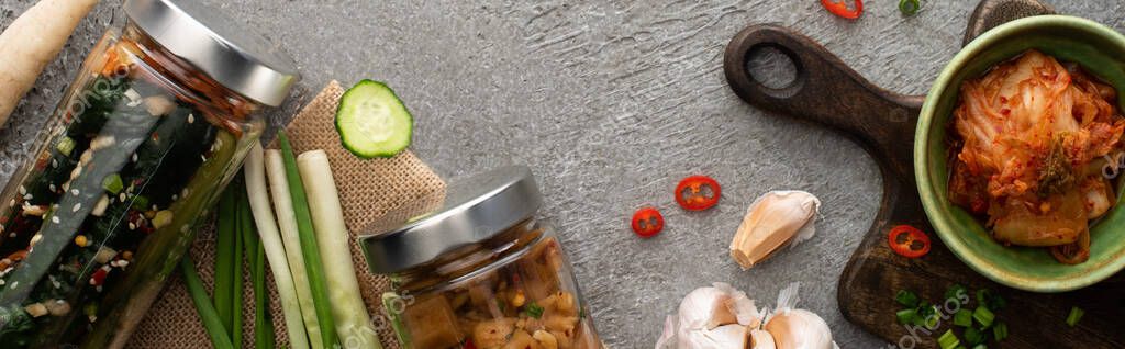 Panoramic shot of tasty kimchi in jars and bowl near garlic and green onions on concrete surface — Stock Image Panoramic Shot Tasty Kimchi Jars Bowl Garlic Green Onions Concrete Stock Picture