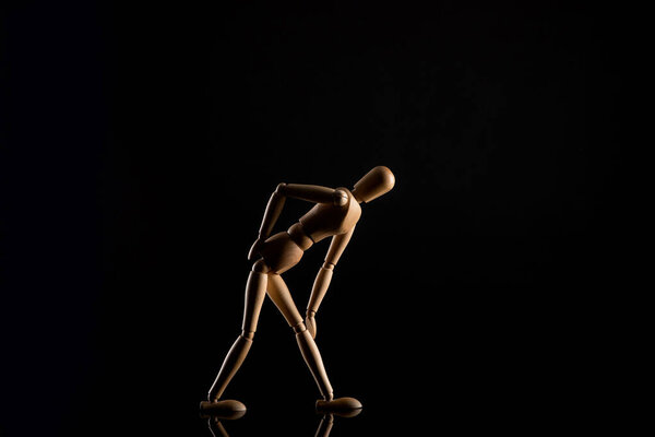 Wooden doll imitating touching knee on black background